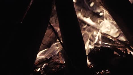 close-up of campfire burning , flames dance and flicker, wooden logs stacked in a teepee formation, sparks flying into the night air, creating warmth and light in the dark environment.