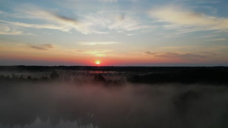 Sunrise-aerial-climbs-over-foggy-lake-revealing-bog-heading-to-horizon