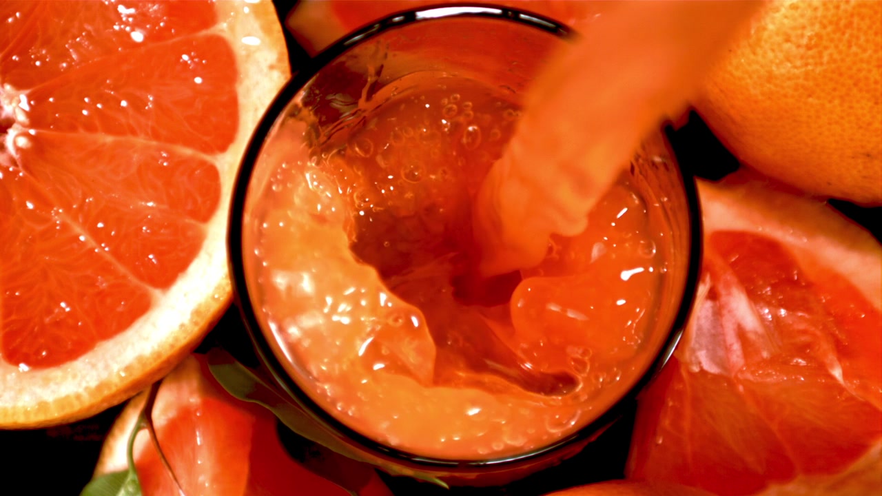 Succo di pompelmo fresco che si versa in un bicchiere con fette di frutta