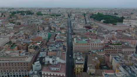 Forwards-fly-above-straight-street-in-urban-borough-on-rainy-day.-Vehicles-driving-between-blocks-of-buildings.-Rome,-Italy