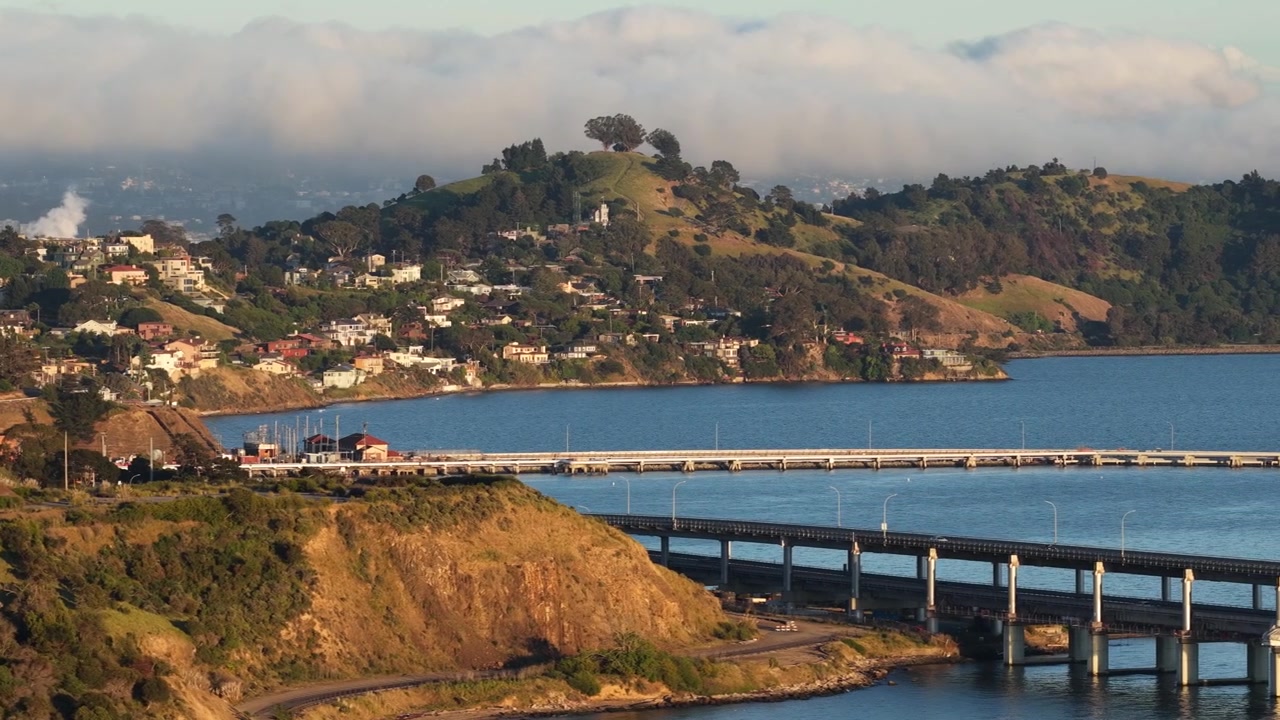 Luftfoto af Richmond-San Rafael Bridge, der strækker sig over San Francisco-bugten ved den gyldne time, med flydende trafik og de disede, skybeklædte bakker i Marin County i det fjerne