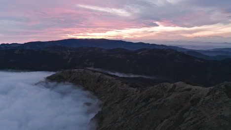 Die-Morgendämmerung-Bricht-über-Nebligen-Bergen-An,-In-Den-Tälern-Liegen-Wolken,-Ruhige-Luftaufnahme