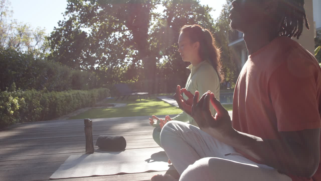 Felice coppia di diverse etnie che pratica yoga e meditazione seduta al sole, spazio per il testo, al rallentatore