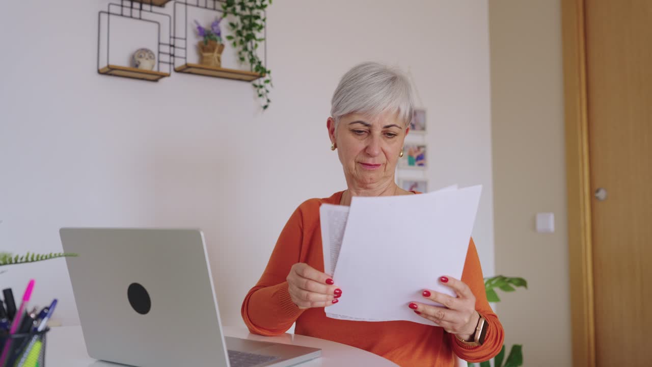 Donna anziana che lavora al laptop ed esamina documenti a casa