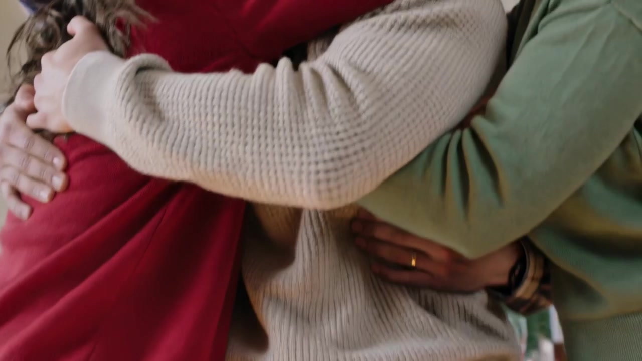 Uomo sorridente con un maglione chiaro che riceve un forte abbraccio di gruppo dopo essersi ritrovati nella zona pranzo, mostrando un anello.