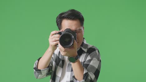 close up of asian photographer using a camera taking picture while standing on green screen background in the studio