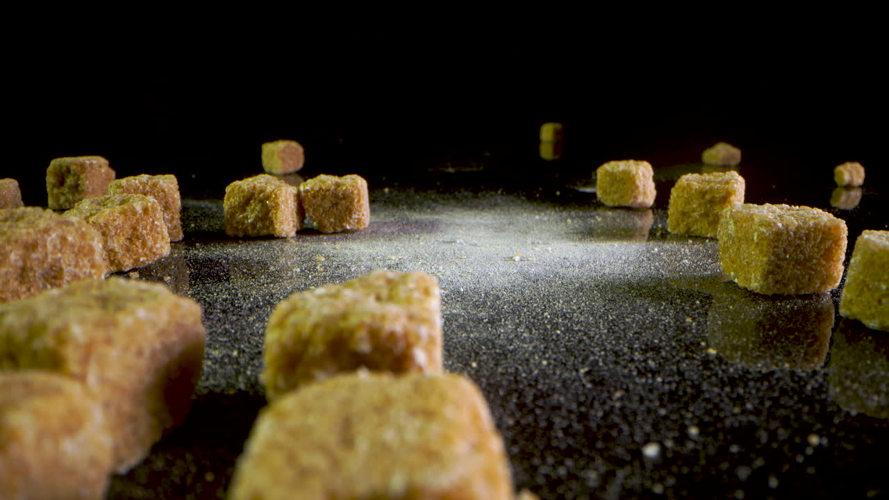 trozos de azúcar moreno cayendo sobre una superficie espejada negra