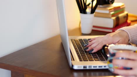 mujer usando una computadora portátil mientras toma una taza de café