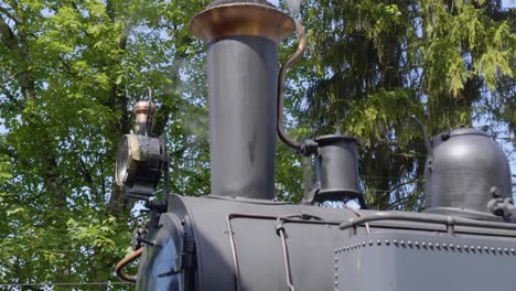 closeup shot on front of steam locomotive, green trees in the background