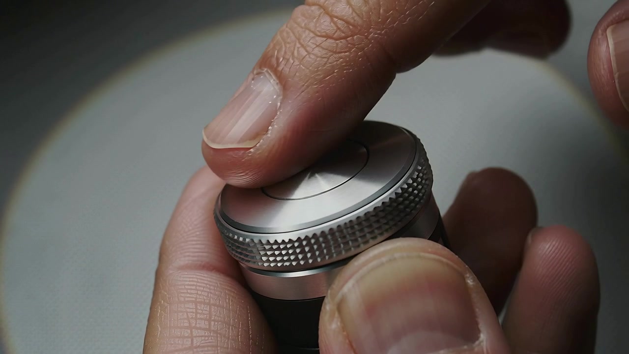 Pressing right index finger on central cap, thumb holding cylinder on workbench