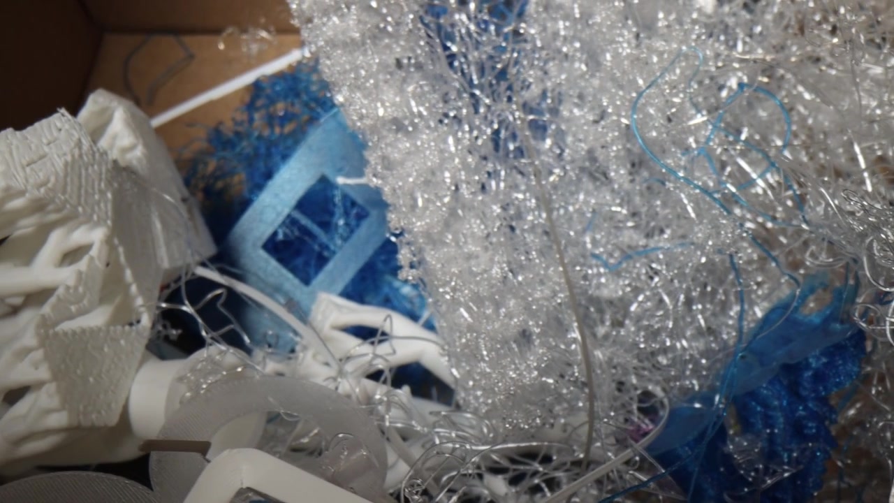 Top-down view of 3D printer waste, featuring flawed prototypes, discarded resin material, and tangled plastic filament strings.