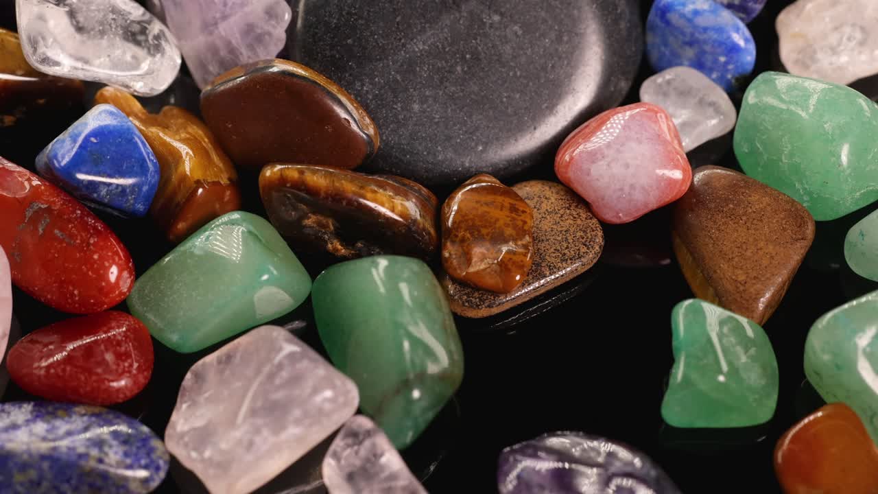Vibrant chakra stones cascade onto a black surface, creating a dynamic and colorful composition with varied lighting and textures