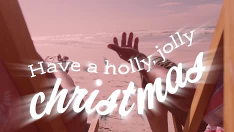 animación de tener un texto de navidad holly jolly sobre una pareja de alto nivel tomados de la mano en una playa soleada