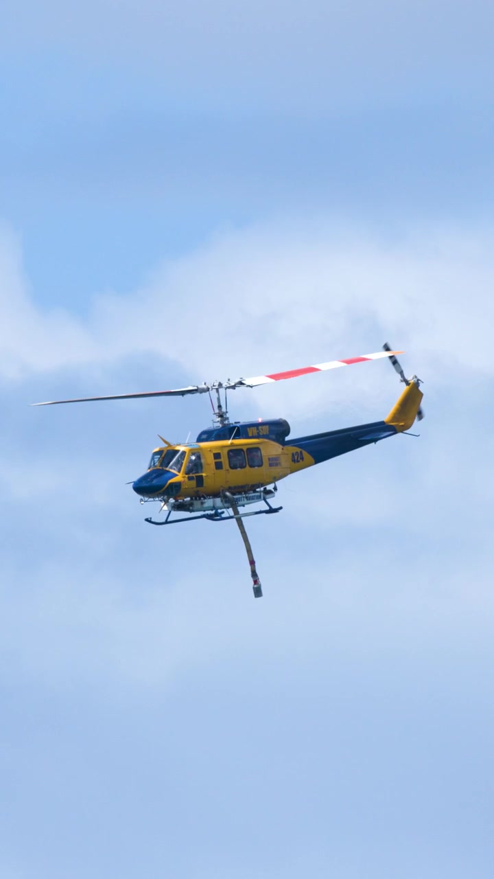 Helicóptero de combate a incêndios amarelo e azul manobra em céus nublados durante o Pacific Airshow, Gold Coast, Austrália
