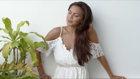feliz morena en vestido blanco de pie junto a la planta verde
