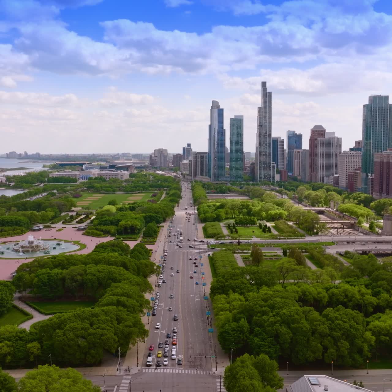 Wide multi-lane road with numerous cars passing through green park zone. Chicago cityscape and skyscrapers at backdrop