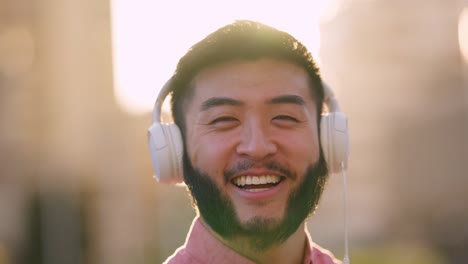 asian man listening to music with headphones smiling to the camera outdoors