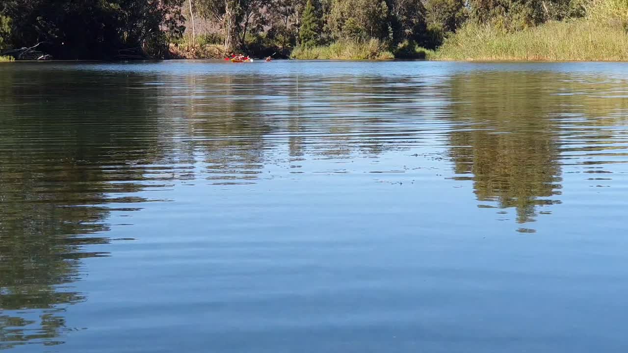 Tourists paddle their canoes in the distance across a shimmering lake