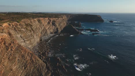 Drohnenaufnahme-Portugiesischer-Klippen,-Die-An-Einem-Sonnigen-Tag-Von-Wellen-Vor-Dem-Atlantischen-Ozean-Umspült-Werden