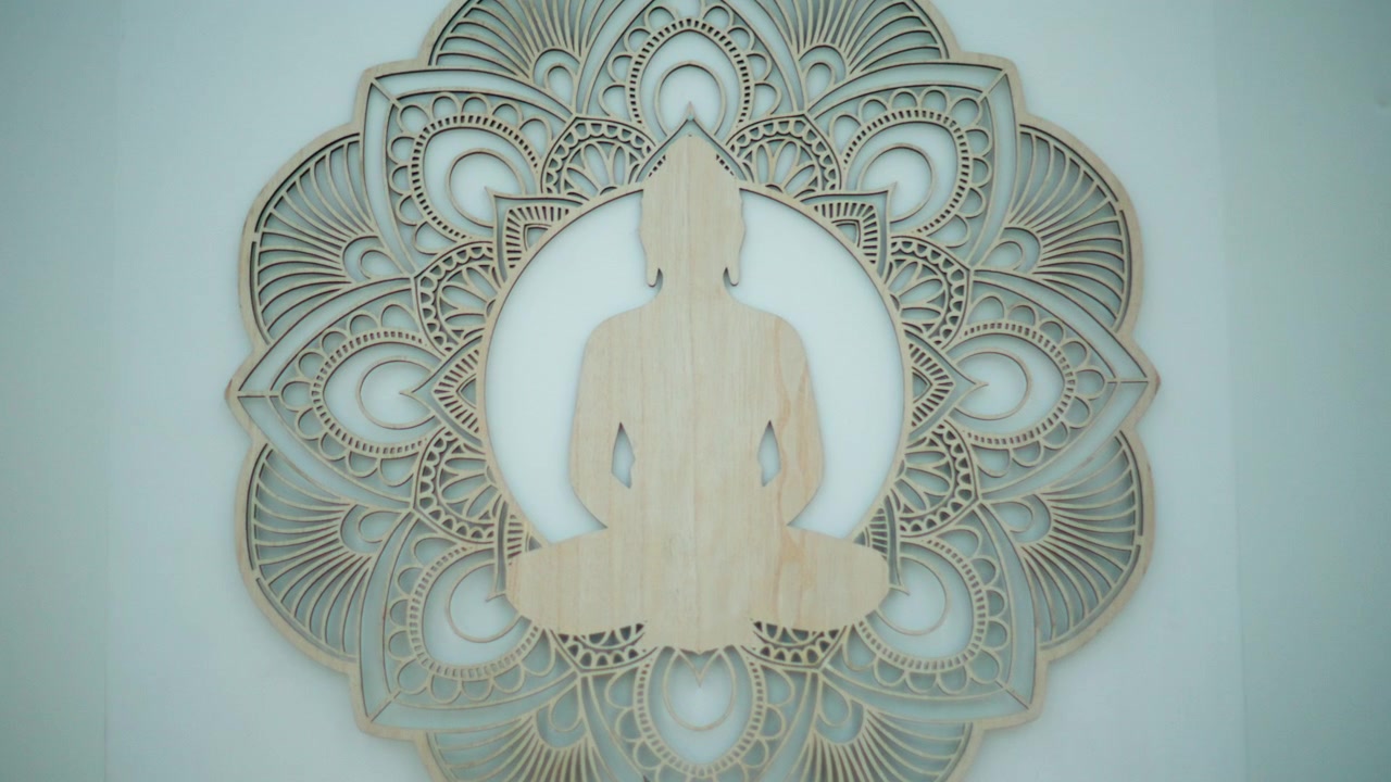 Buddha-silhuet udskåret i træ, siddende i meditationsstilling, centreret på en lagdelt mandala vægdekoration.