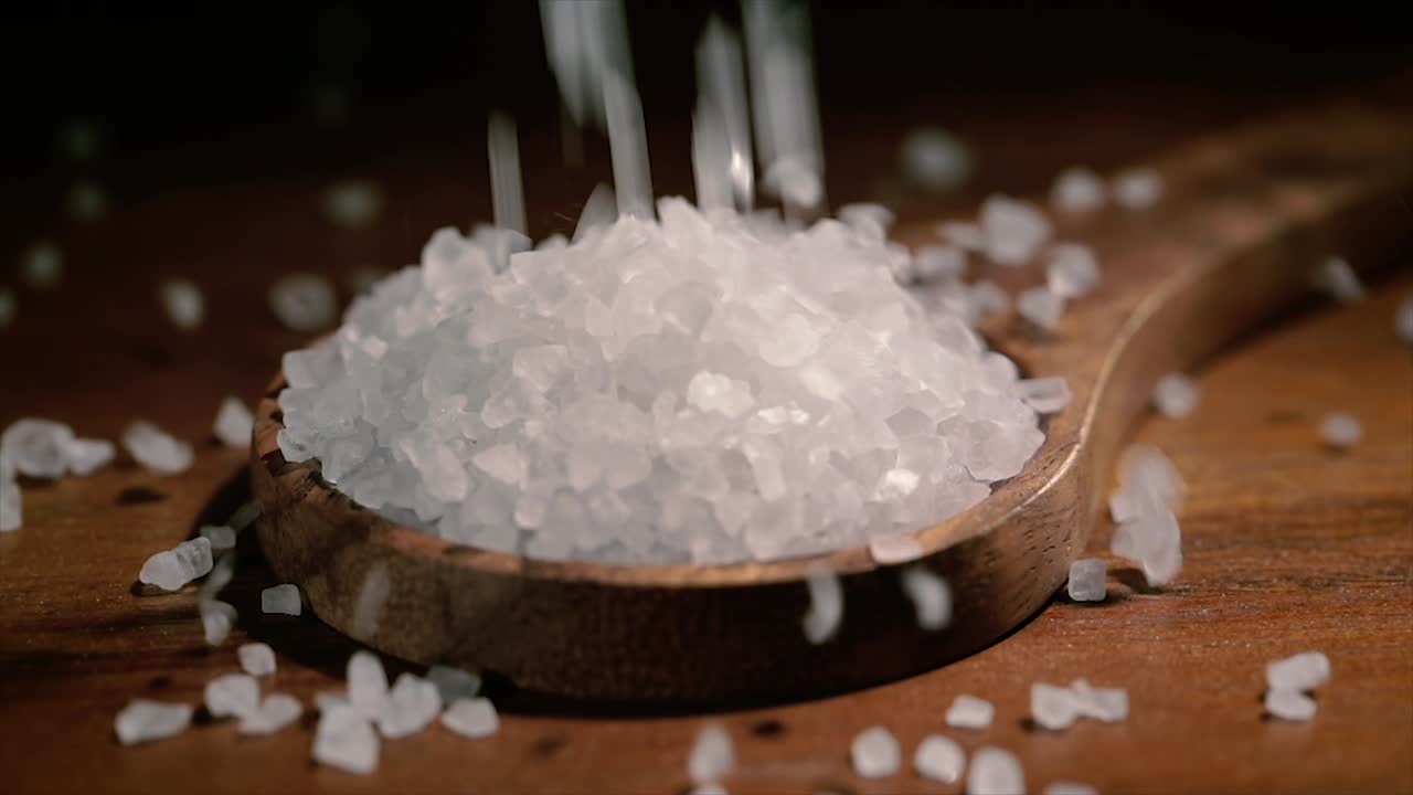 Sea salt crystals closeup in wooden spoon on a kitchen table.