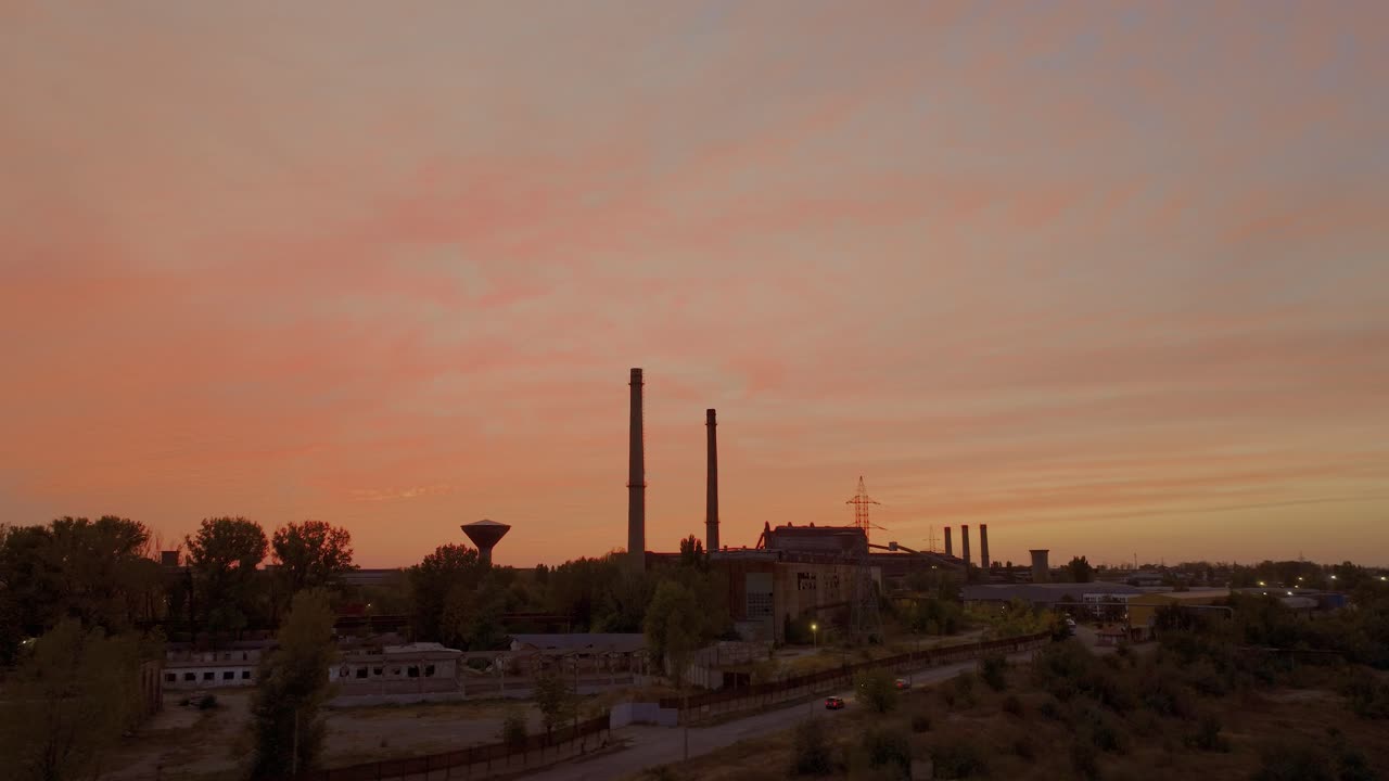 aeria seguimiento de una toma de un cálido abrazo de una impresionante puesta de sol ilumina una zona industrial desgastada por el tiempo y las siluetas de los altos hornos de pie centinela 4k50fps grado cinematográfico