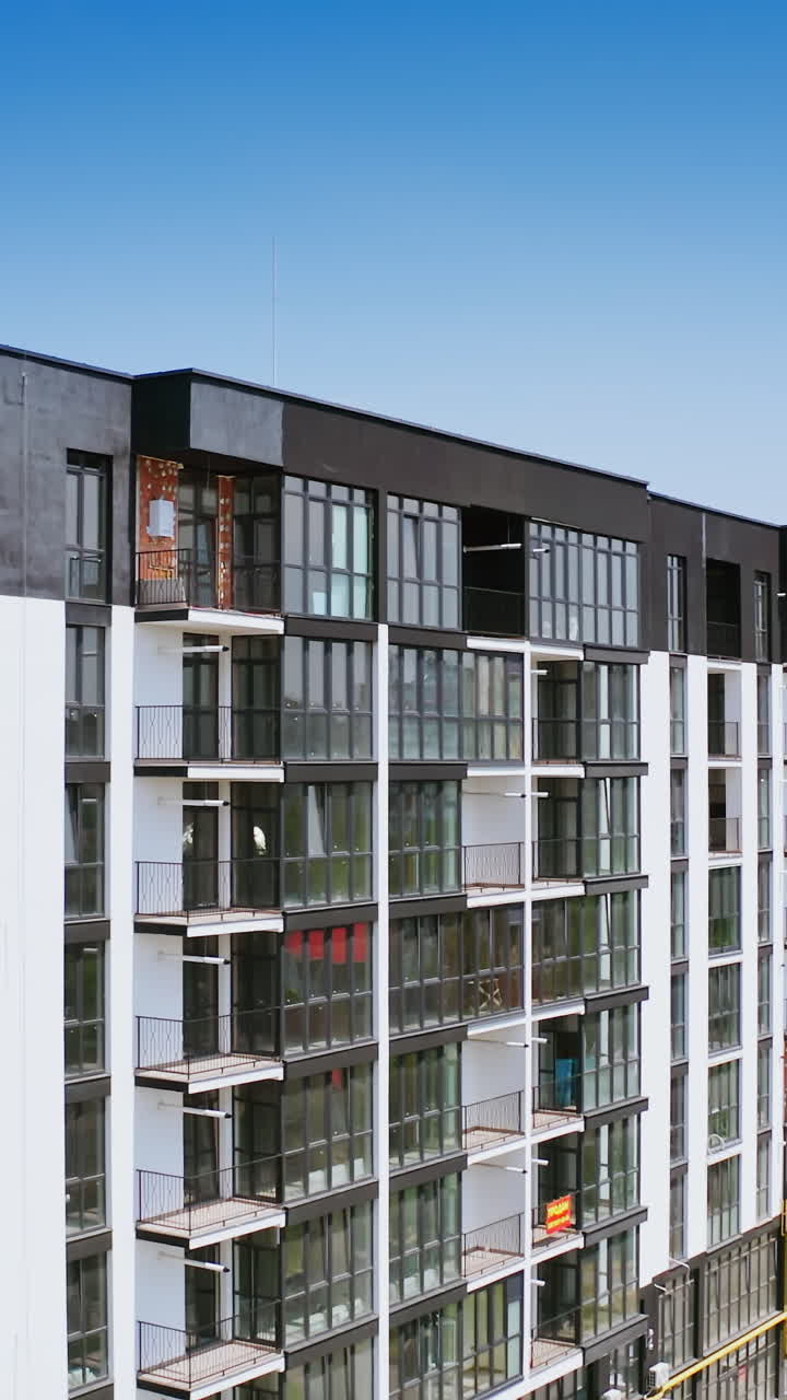 New highrise building in the city street. Modern design of newly built apartment building with large glassed balconies on urban background. View from the air. Vertical video