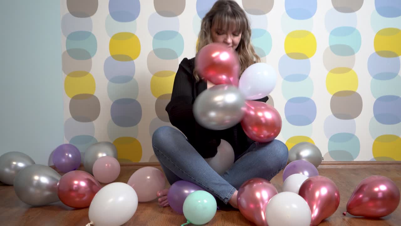 mujer joven sentada alrededor de globos y jugando con globos contra un fondo colorido