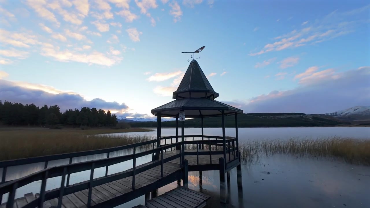 Ihmisiä kävelemässä puulaituria pitkin kohti huvimajaa Laguna La Zetassa, Argentiinassa. Pehmeä auringonlaskun valo valaisee järven ja kaukaiset vuoret.