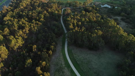 Vista-Suave-De-Drones-Del-Camino-Del-Parque-Al-Lado-De-La-Carretera-Concurrida-Y-El-Estadio-Deportivo