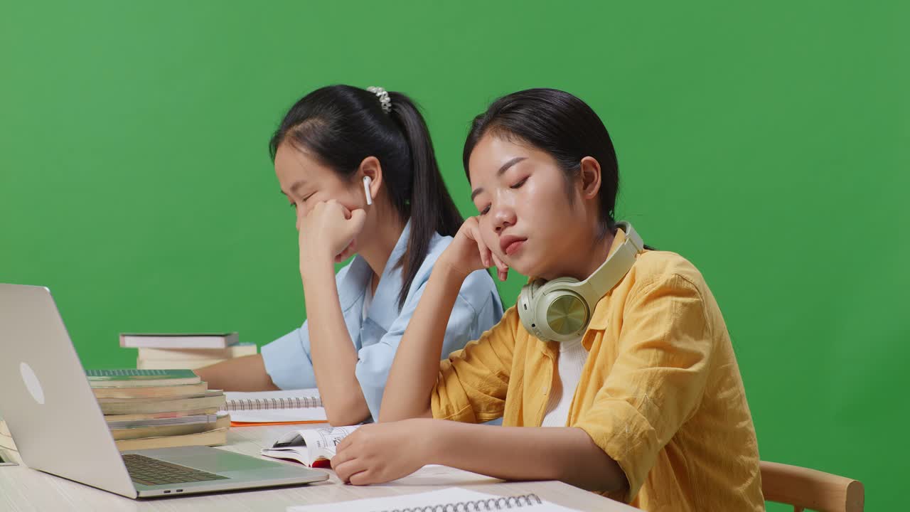 아시아 여성 학생들이 녹색 화면 배경 교실에서 노트북과 함께 테이블에 앉아 책을 읽는 동안 지루합니다.