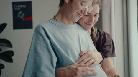 lesbian family couple waiting for a baby, hugging and smiling at home