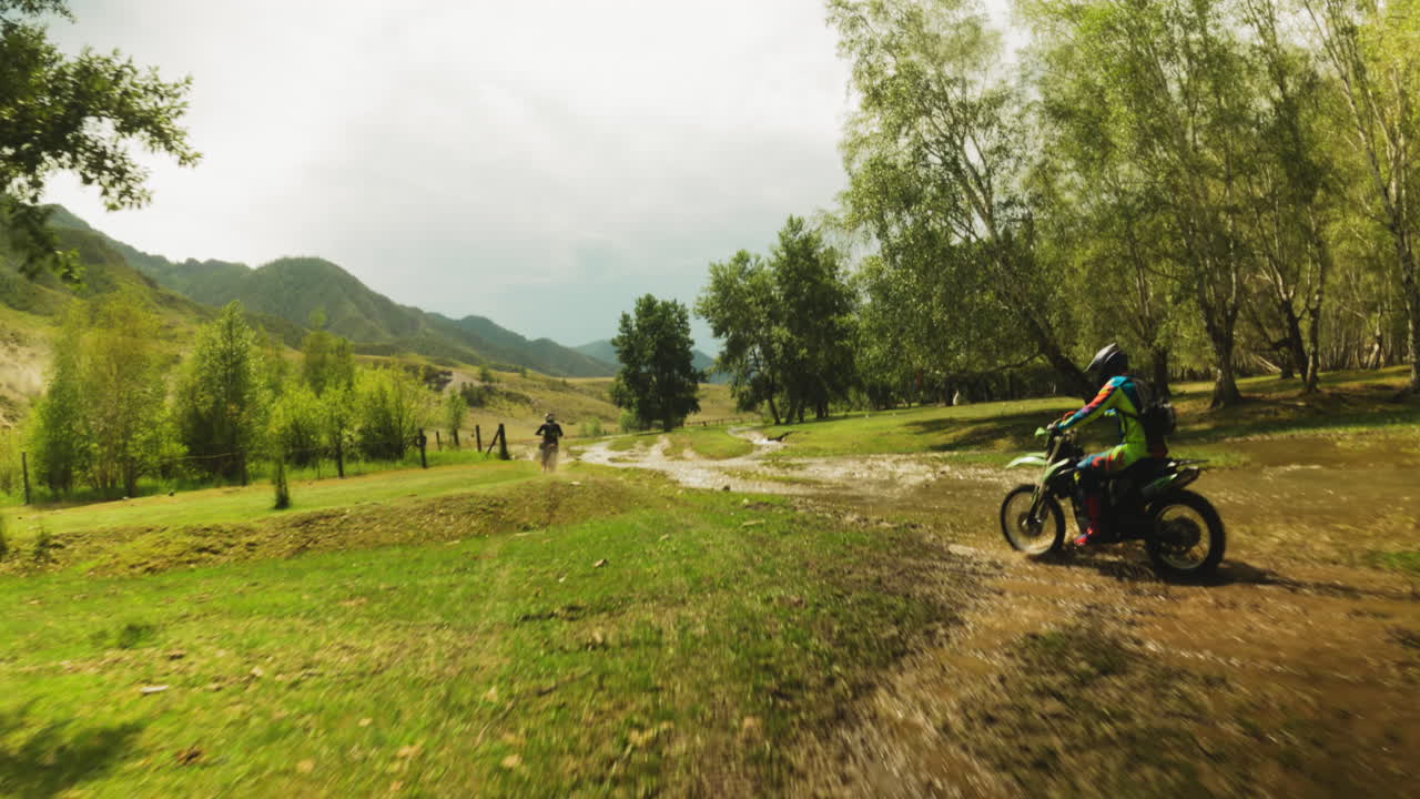 Sportivi in moto attraversano un boschetto con un ruscello in gara FPV. Motociclisti su veicoli potenti competono in guida estrema nella natura selvaggia. Gara di motocross
