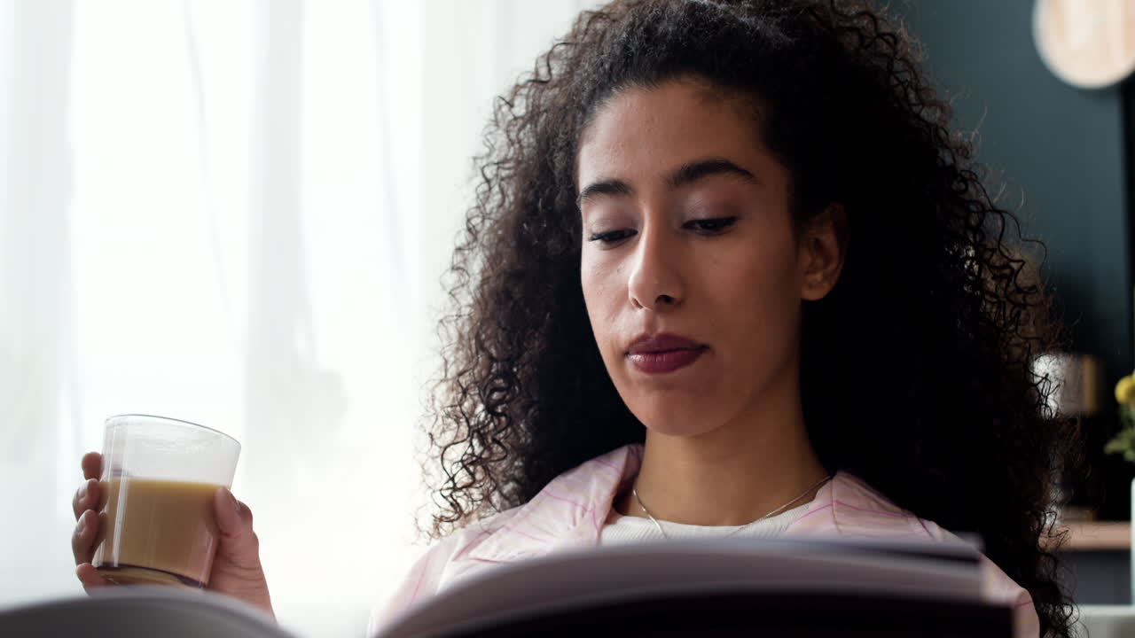 Young woman drinking coffee and reading a book at home
