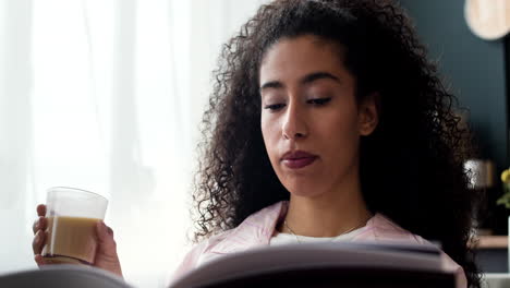 young woman drinking coffee and reading a book at home