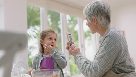 happy-grandmother-using-smartphone-taking-photo-of-cute-grandaughter-in-kitchen-mixing-ingredients-for-baking-tasting-chocolate-sauce-granny-sharing-weekend-with-grandchild-on-social-media