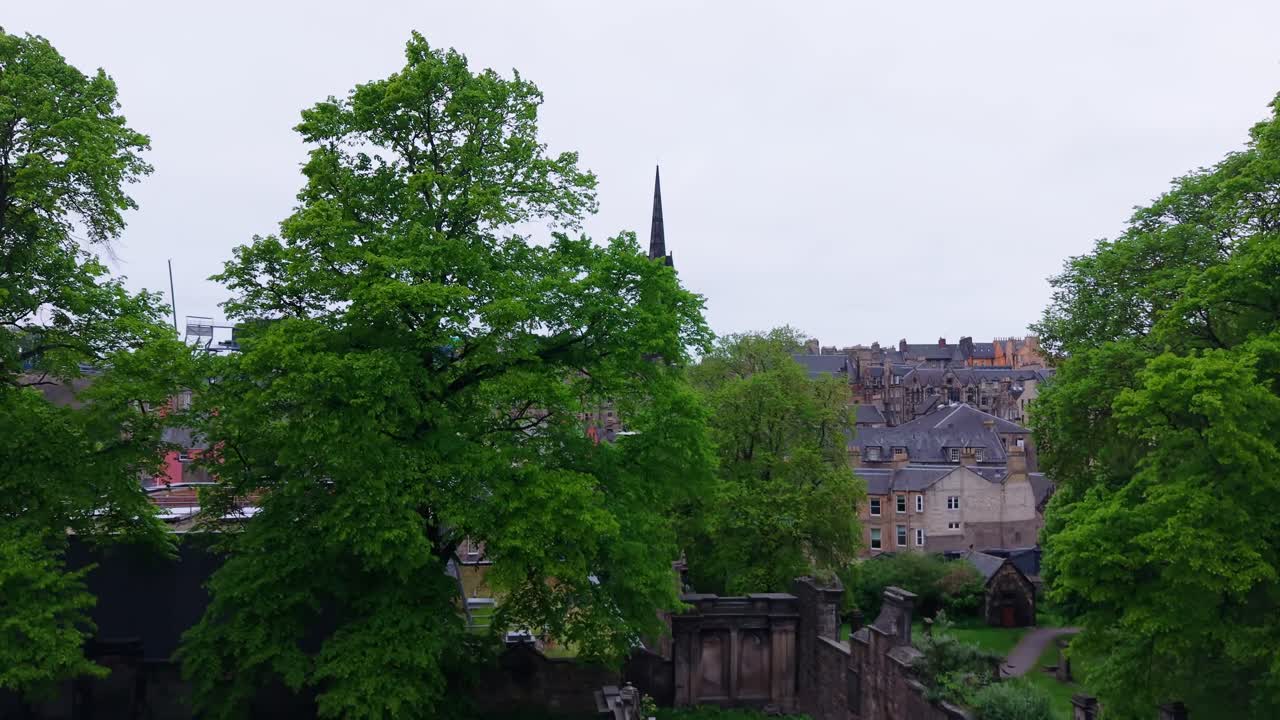 Aerial cinematic reveal of Edinburgh with the dramatic gothic spire of Tolbooth Kirk rising above the historic skyline. Stunning architecture in a moody atmosphere