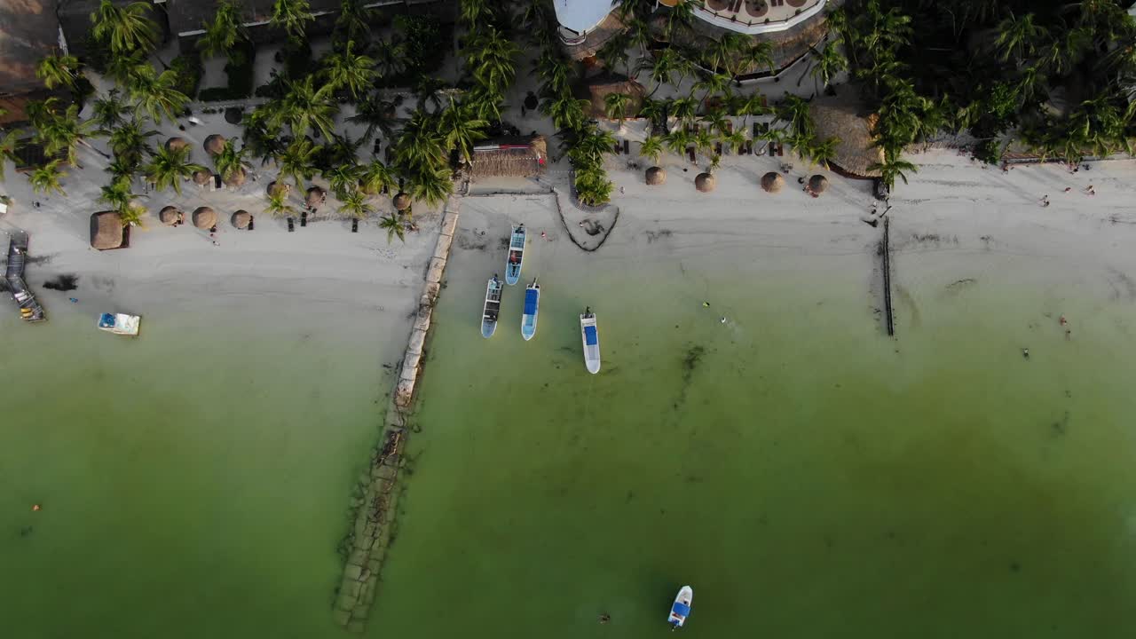 Bird’s eye view ascending shot, pump boats on the shoreline of Isla Holbox, Mexico, Scenic view of green water, palm tree and houses in the background