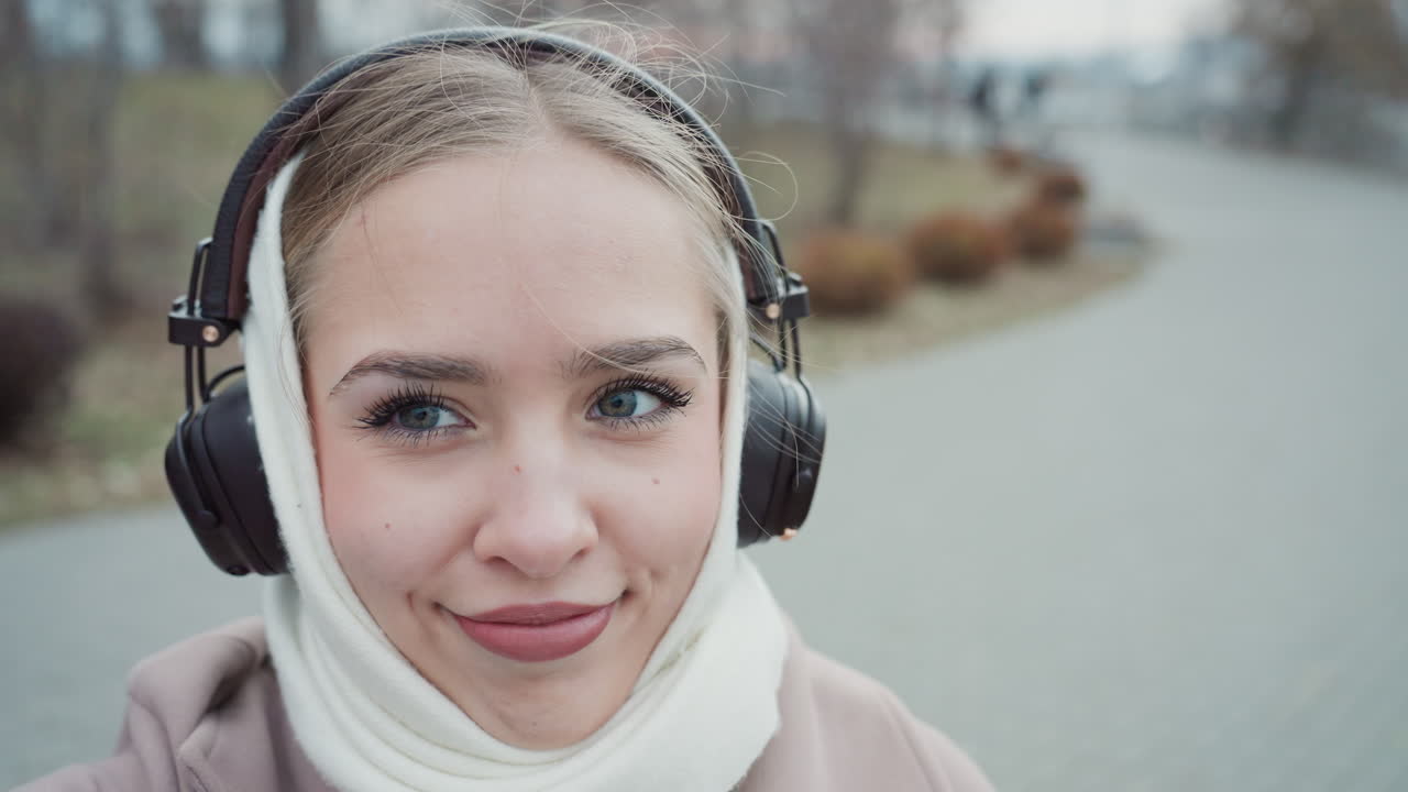 Donna sorridente si immerge nella musica all'aperto. Donna ascolta felicemente musica durante una passeggiata all'aperto fredda. Donna con le cuffie sorride mentre si gode le melodie durante le fredde passeggiate all'aperto.
