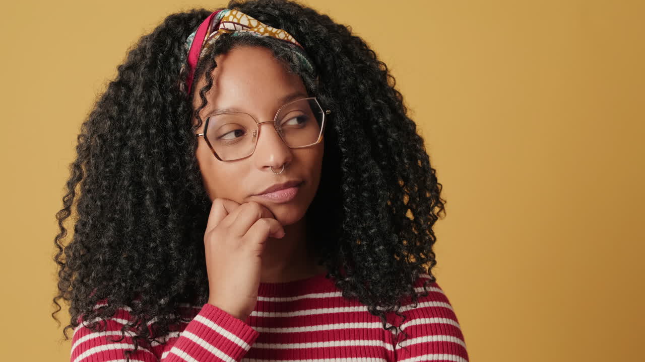 Thoughtful Young Woman with Curly Hair Pondering on Yellow Background
