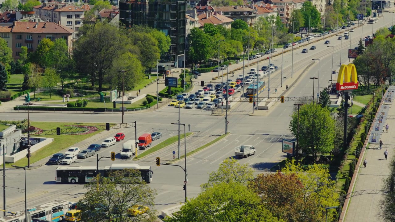 Forhøjet udsigt over travl bytrafikkryds ved NDK Park med biler, busser og grønt i Sofia.