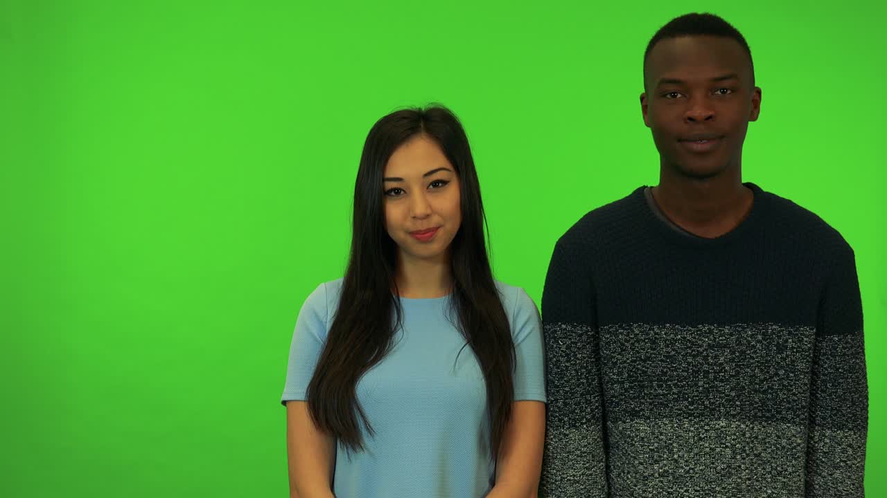 A young Asian woman and a young black man applaud and nod their heads appreciatively - green screen studio