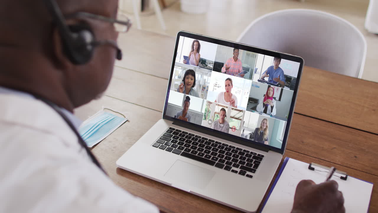 African american male doctor taking notes while having a video conference on laptop