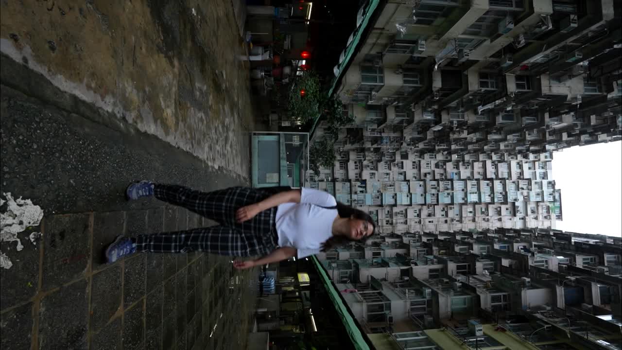 Woman walks backwards looking at Monster Building in Hong Kong. Vertical
