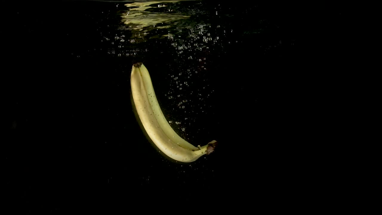 un plátano amarillo maduro fresco que cae en el agua clara