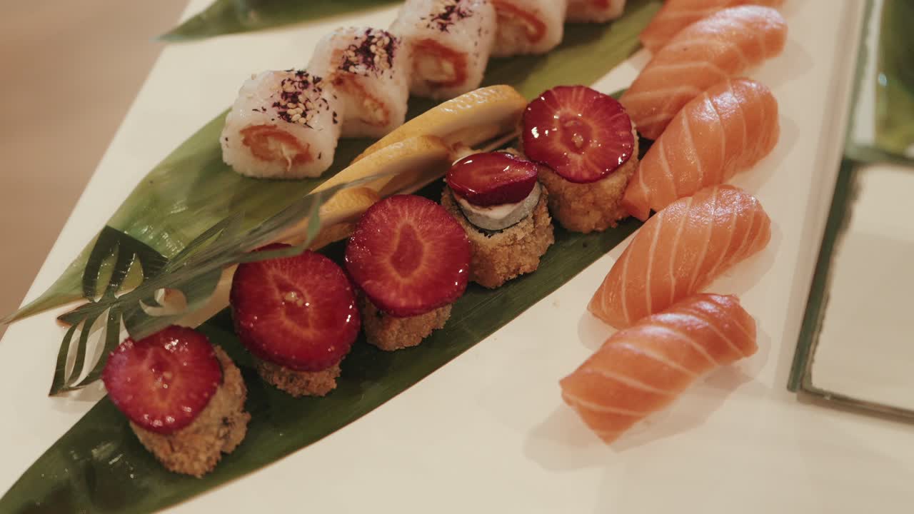 close up of strawberry topped sushi rolls beside fresh salmon nigiri on white platter