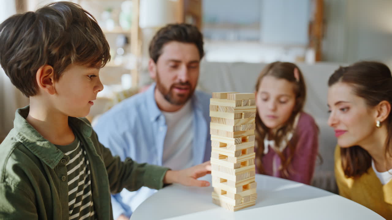 Primo piano di una famiglia felice che gioca a Jenga e si gode il tempo libero in casa. Un bambino cerca di mantenere l'equilibrio