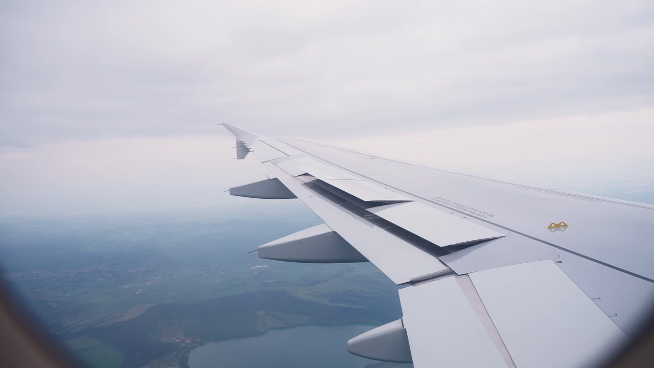 Passenger window view moving toward an airplane wing during descent, capturing a handheld in-flight travel perspective above a hazy landscape.