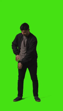 vertical video full length shot of man looking at text message on mobile phone standing against green screen