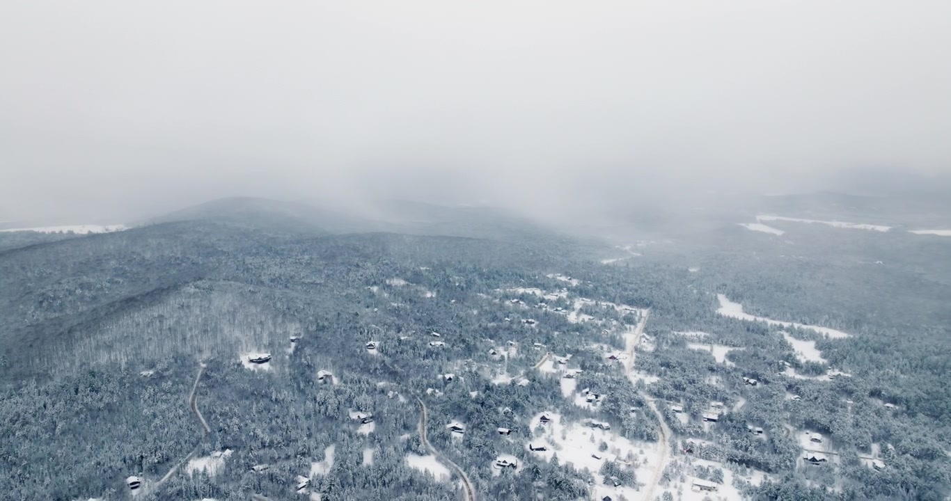 Drohne fliegt hinaus und enthüllt ein schneebedecktes Wohngebiet in den Adirondacks mit Häusern, die im dichten Wald verstreut sind, während tiefe Winterwolken über der Landschaft nahe Lake Placid, New York, hängen.
